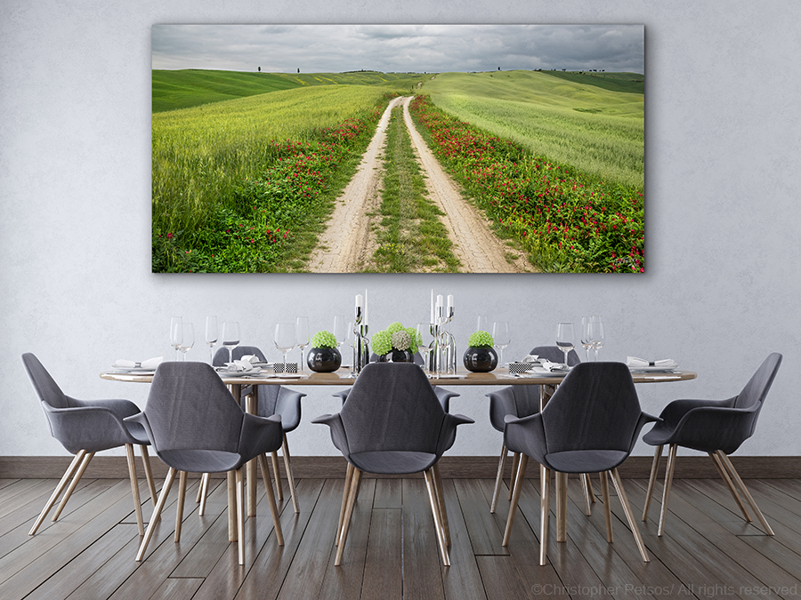 A white road of Tuscany photographed by Christopher Petsos, with green fields of wheat on both sides as far as the eye can see